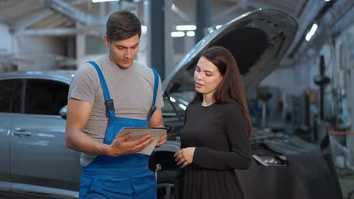 Konzentrierter kaukasischer Mann erklärt einer zufriedenen Frau, die drinnen beim Service steht, die Autoreparatur