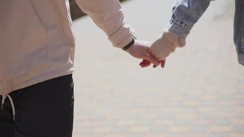 Woman in Jacket Holds Finger of Strong Man in Hoodie While Walking on Street