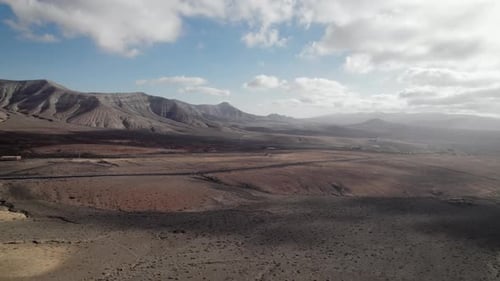 aerial shot of desert valley with mountain range on an island with desolate landscape and partly clo