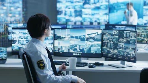 In the Security Control Room Officer Monitors Multiple Screens for Suspicious Activities. He's Surr