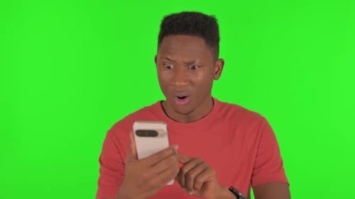 Portrait of African Man Shocked by Loss on Phone on Green Background