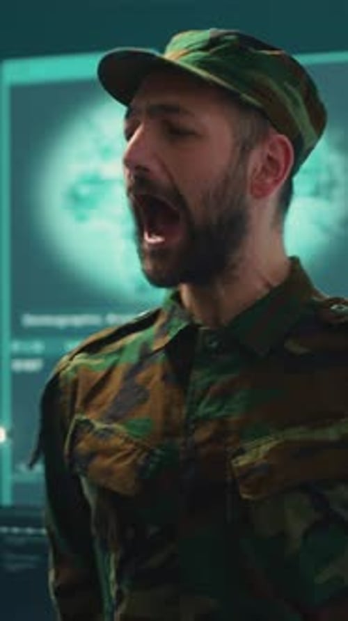 Man in Camouflage Uniform Speaking Near Computer Screens