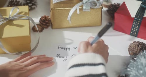 Close up of girl hands writing greeting card winter christmas decorations on table.