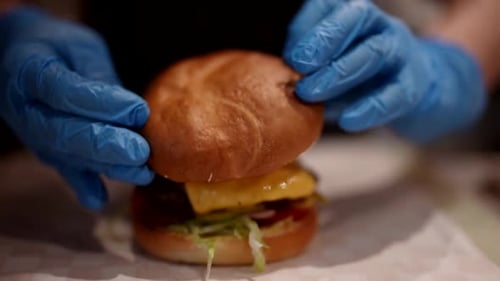 Cook Assembling and Packing Hot Tasty Burger with Beef Cutlet and Cheese Closeup View Fast Food