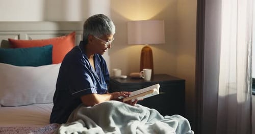 Senior Woman Reading Book on Bed