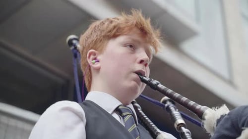 Young street performer with ginger hair playing his bag pipes