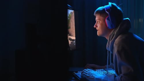 Konzentrierter junger Cybersportler mit Kopfhörern spielt im FPS-Videospiel auf dem PC in