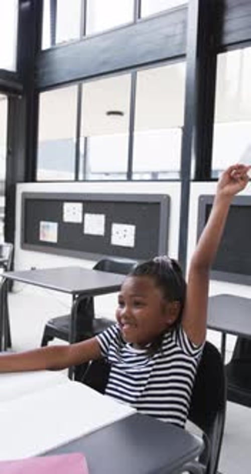 Vertical video: In a school setting, an African American young girl raises her hand
