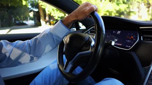 Male Hand of Businessman Holds Steering Wheel While Driving Electrical Vehicle at City