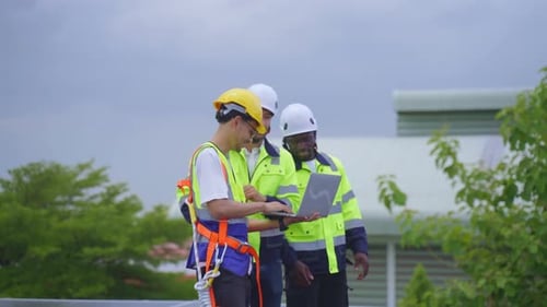 Engineers Inspecting Solar Panels on Rooftop with Laptop