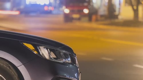 Close Up of Parked Car on Roadside at Night with Blurred View of Traffic Lights of Moving Vehicles