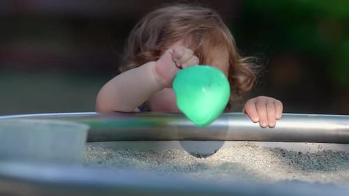 Child Plays with Toy in Sandbox at Playground