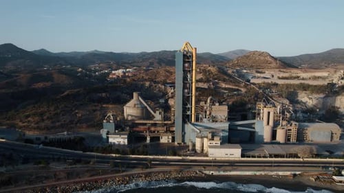 A slow cinematic aerial view of a Cement Factory known for its pollution in the nearby popular touri