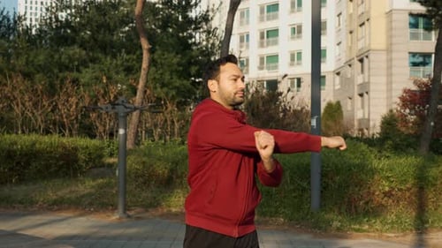 Bearded man stretching arms in an outdoor apartment park before race or marathon training workout. C