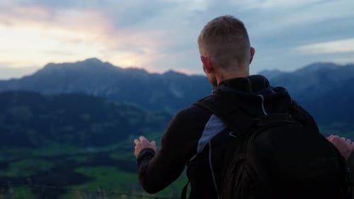 Hiker Pointing At Blurry Mountain Landscape During Sunset