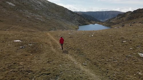 Man on a red coat walking on the mountains arriving to a beautiful little lake in Puymorens