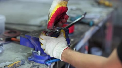 Man is Working with a File a Rasp a Metal Spare Part is Clamped in Vice on a Workbench in Workshop