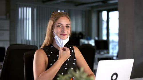 Young businesswoman takes off face mask in office after coronavirus pandemic