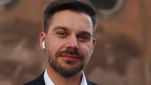 Portrait View of the Handsome Man Wearing Earphones Looking at the Camera with Pleasure Smile While