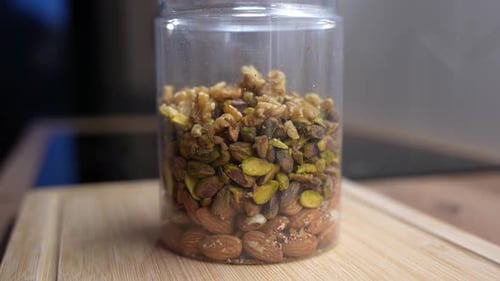 Mixed nuts falling into plastic jar