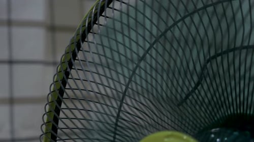 an old green fan rotating to cool the room with a grid curtain as a background