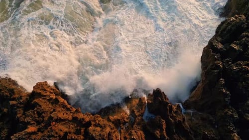 Foamy sea waves splashing on volcanic stones seashore swirling slow motion aerial top view