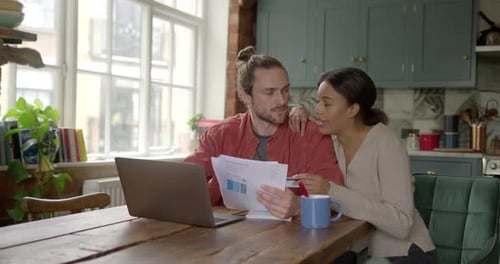 Young Couple Looks at Laptop and Documents at Home