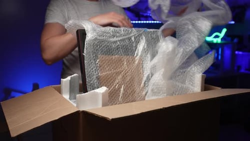Vue avant recadrée d'un homme méconnaissable déballant une boîte en carton avec un nouveau moniteur de jeu enveloppé