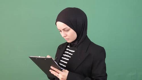 Woman in Hijab Writing on Clipboard Against Green Screen