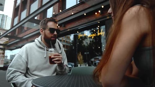 Attractive young couple having lunch sitting at cafe table outdoors, drinking coffee and talking
