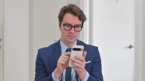 Excited Man Celebrating Success with Smartphone Indoors
