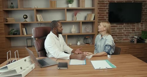 Black Doctor Measuring Blood Pressure to a Young Woman at Office