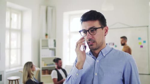 Young businessman in modern office talks on smartphone with colleagues