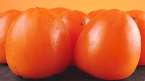 Frische reife Kakifrüchte rotieren auf einem Steinbrett auf pfirsichfarbenem Hintergrund.