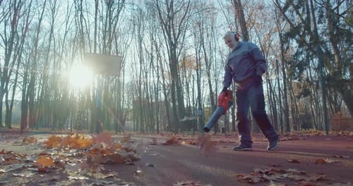 Un concierge nettoie le parc municipal d'automne avec un souffleur à feuilles