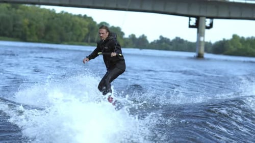 Man Wakeboarding on River Waves Under City Bridge in . Rider