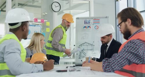 Multiracial team of engineers and chiefs revision ready building drawing during briefing in meeting