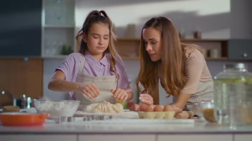 Woman Teaching Girl To Prepare Dough For Cookies On Modern Kitchen. Small Daughter Kneading Dough...