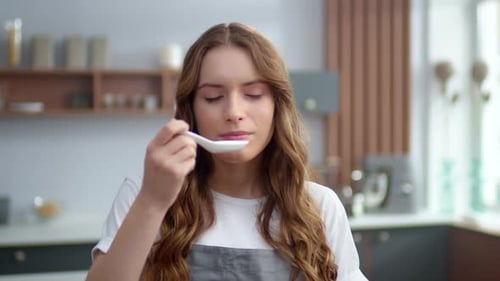 Woman Tastes Food From Spoon in Kitchen
