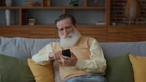Senior Man Relaxing at Home Using Smartphone