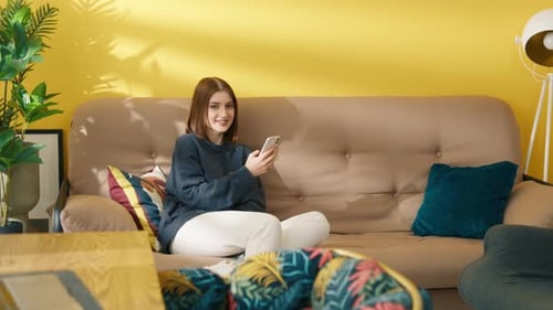 Young Woman Using Smartphone on Sofa at Home