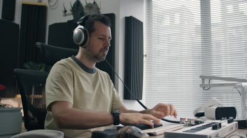 Man creating music at home, focused on his computer and keyboard in a modern home studio