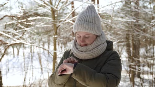 Woman Checks Smart Watch in Snowy Winter Forest
