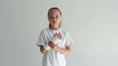 Studio Portrait of Sad Cute Little Girl Massaging Forearm with Expression of Pain on Face Looking at