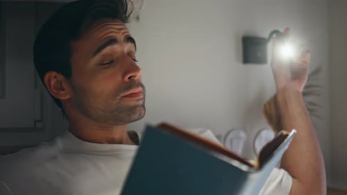 Man Reading Book Under Lamp Light at Night
