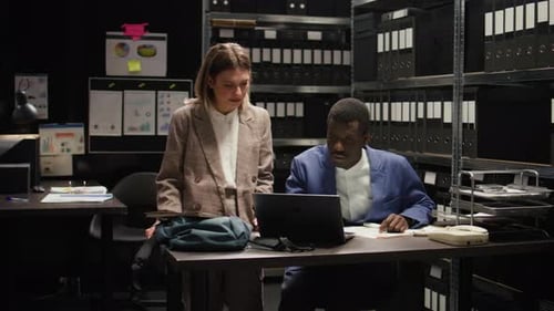 Coworkers Reviewing a Laptop Together in Darkened Office