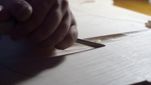 Luthier is using a chisel to carefully carve a piece of wood for a new violin in his workshop.