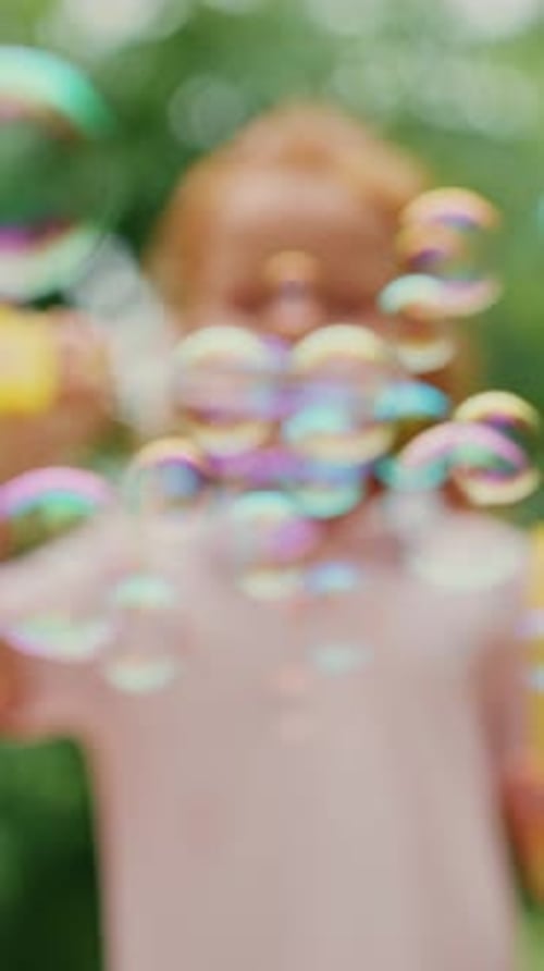 Young Girl Blows Bubbles in a Park Surrounded By Greenery on a Sunny Day