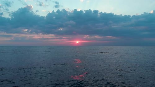Aerial shot of the red sun rising among clouds and creating light streaks on the sky at sunrise