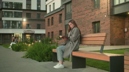 Young Lady Reading Book on Bench Near Residential Building